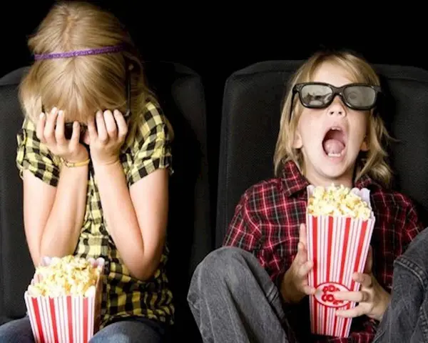 Dzieci w kinie, kiedy pierwszy raz do kina z dzieckiem. Jedno zakrywa twarz, drugie z popcornem w szoku.
