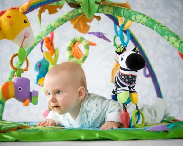 Maluch odkrywa świat na kolorowej macie edukacyjnej dla dzieci. Wesołe zabawki zachęcają do zabawy.