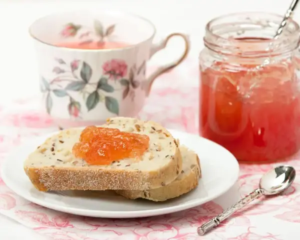 Fetta di pane con marmellata di anguria, tazza da tè fiorita e barattolo di marmellata.