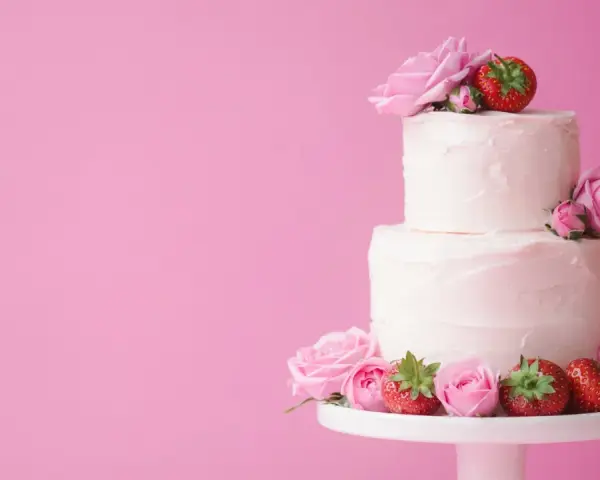 En vacker tvåvåningstårta med rosa frosting, dekorerad med rosor och jordgubbar. Perfekt för ett sommarbröllop eller en fest. Ett enkelt tårta recept att följa.
