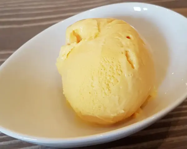 Ein Löffel cremiges, gelbes balla balla Eis in einer weißen Schale auf Holzhintergrund.