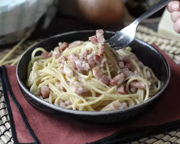 Un tenedor recoge espaguetis cremosos con trozos de bacon crujiente, creando un delicioso plato de pasta con bacon.