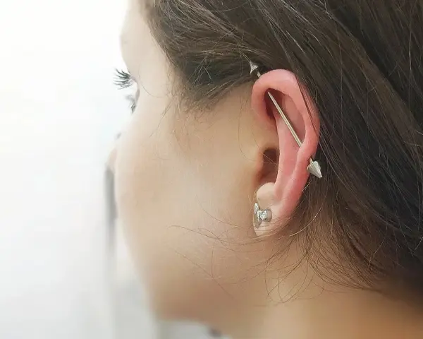 Industrialny piercing ucha z długą sztangą i dwoma stożkami. To przykład, co to jest piercing, który ozdabia ciało.