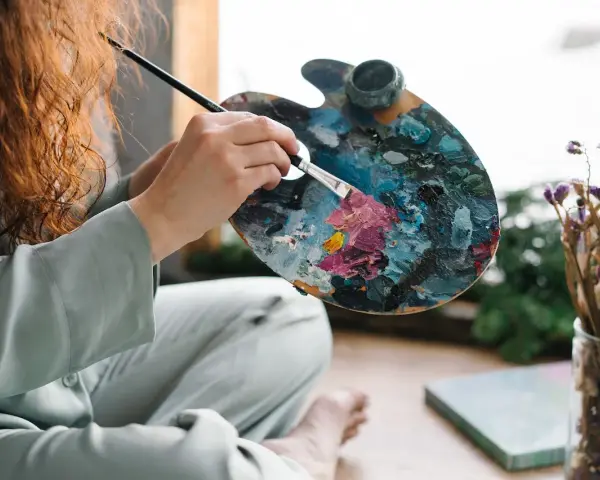 Une artiste aux cheveux roux mélange des couleurs vives sur sa palette, prête à peindre. Apprenez comment utiliser la peinture acrylique pour créer de telles œuvres.