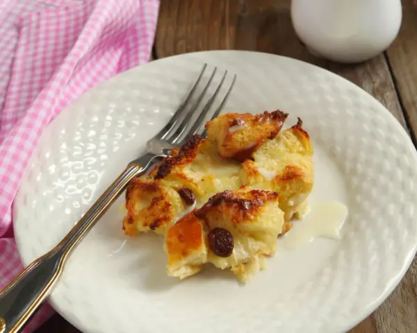 Brotpudding mit Rosinen auf einem Teller mit einer Gabel und einer rosa karierten Serviette.