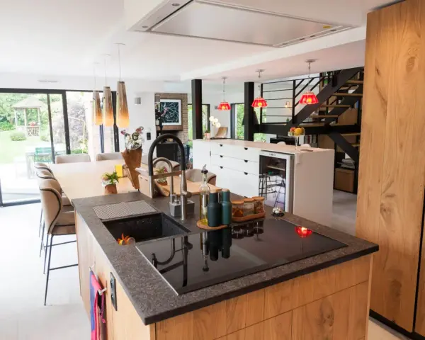 Îlot de cuisine moderne avec plan de travail en granit, évier noir et plaque à induction. La **rénovation cuisine bois massif** se révèle dans les placards et l'îlot central.