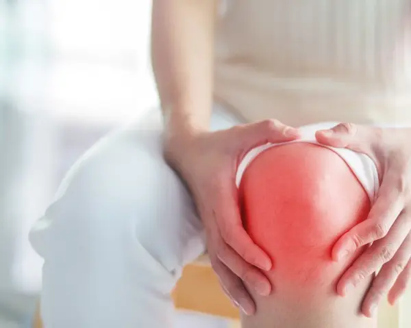 Hände umfassen ein schmerzendes Knie, das rot aufleuchtet, ein Zeichen für Arthrose im Knie.