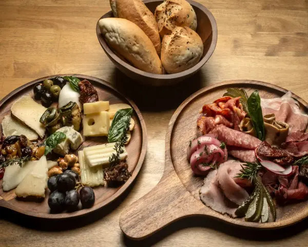 Deska serów i wędlin inspiracje: bogactwo smaków i aromatów na drewnianych deskach, z pieczywem w tle.