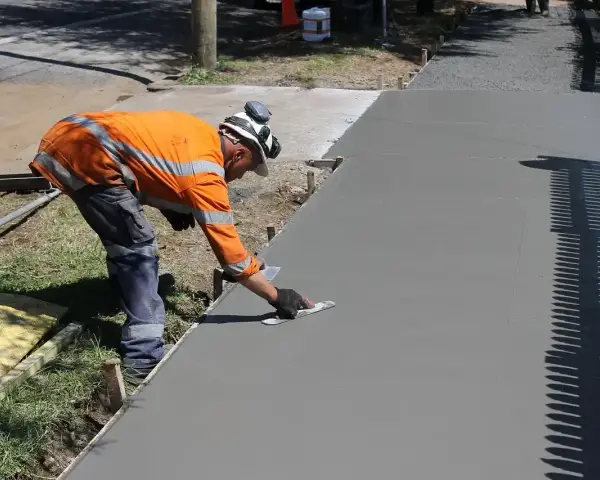 Robotnik w pomarańczowej kamizelce wygładza świeży beton. Zastanawiasz się, ile kosztuje kubik betonu na taki podjazd?