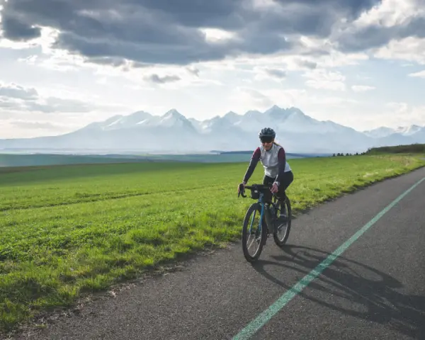 Kobieta na rowerze pokonuje malowniczą trasę z widokiem na ośnieżone Tatry. To wyzwanie: rowerem dookoła Tatr w jeden dzień!