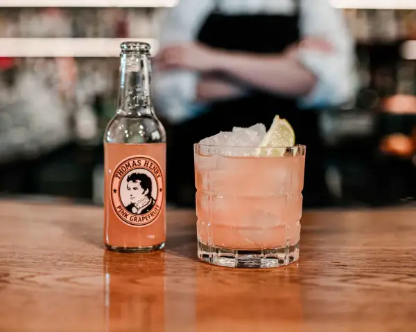 En rosa tequila drink med is och lime, bredvid en flaska Thomas Henry Pink Grapefruit.