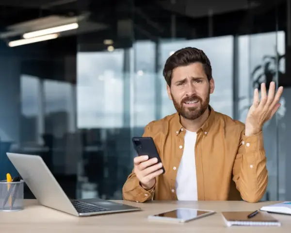 Zdezorientowany mężczyzna trzyma telefon, jakby właśnie dowiedział się o problemach z cesją.