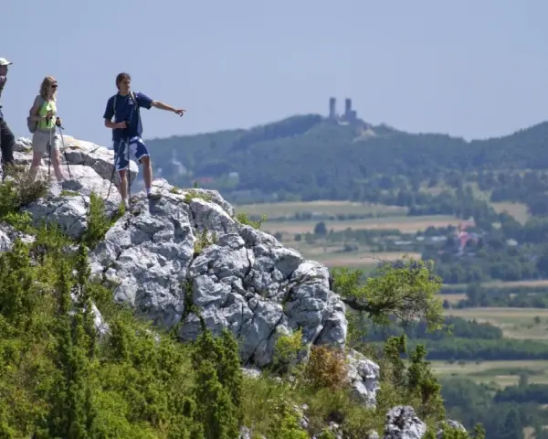 Trzech turystów na skalistym szczycie, wskazując na ruiny zamku w oddali. Piękne krajobrazy gór Kielc.