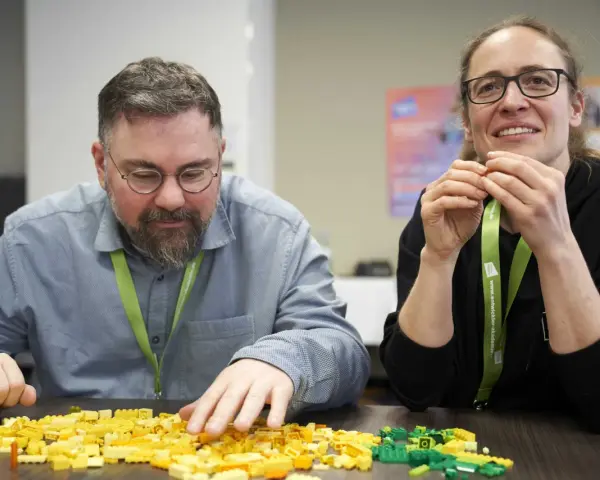 Zwei Personen bauen mit bunten Legosteinen, während sie an einem software architecture summit teilnehmen.