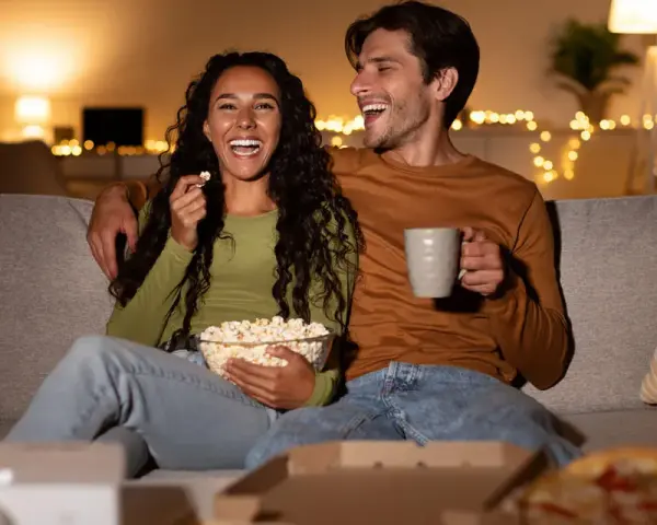 Ein lachendes Paar genießt einen gemütlichen Filmabend mit Popcorn und Pizza. Perfekte filmabend snacks für einen entspannten Abend.