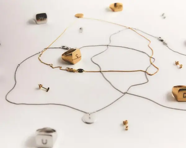 Joyas con letras, como limpiar la plata para que brillen. Anillos y collares dorados y plateados sobre fondo blanco.