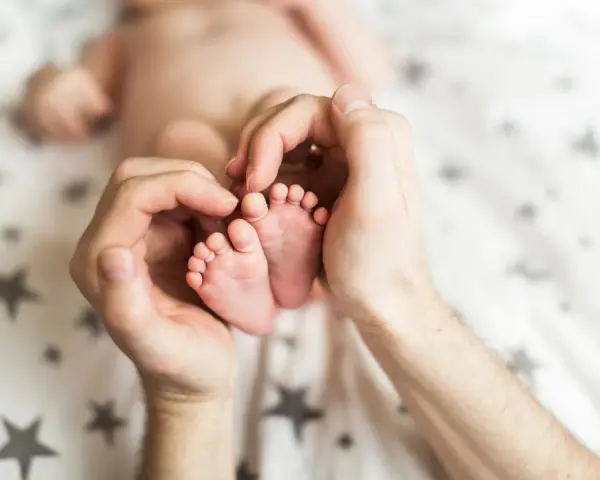 Dłonie obejmujące stópki 7 tygodniowego dziecka. Delikatne paluszki i pięty maluszka otoczone troską.