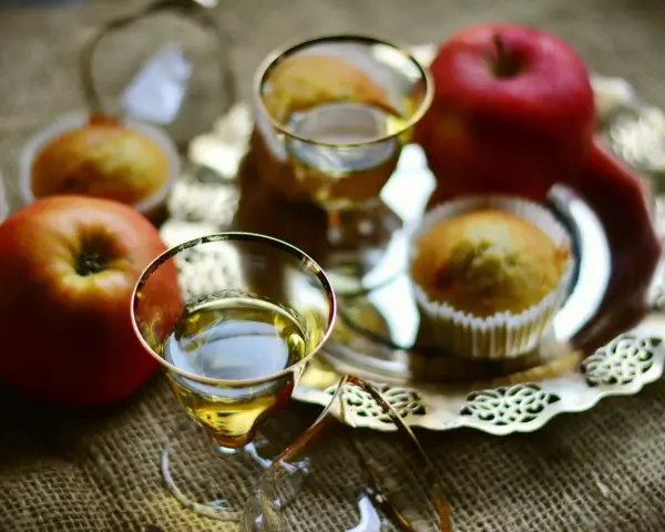 Zwei Gläser mit goldenem Schnaps, Äpfel und Muffins auf einem Silbertablett. Perfekt für den Genuss von selbstgemachtem Kartoffelschnaps.