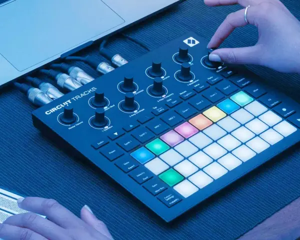 Ręce tworzą muzykę na Novation Circuit Rhythm, z podłączonym laptopem i kablami.