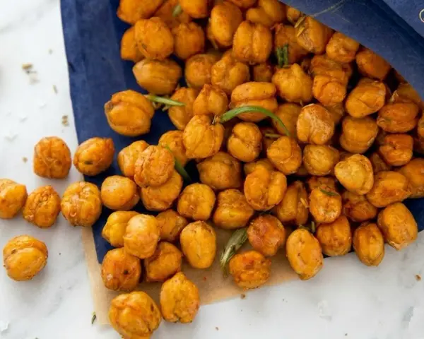 Un sacchetto blu rovesciato rivela una montagna di ceci croccanti al forno, dorati e invitanti, con qualche rametto di rosmarino sparso tra loro.