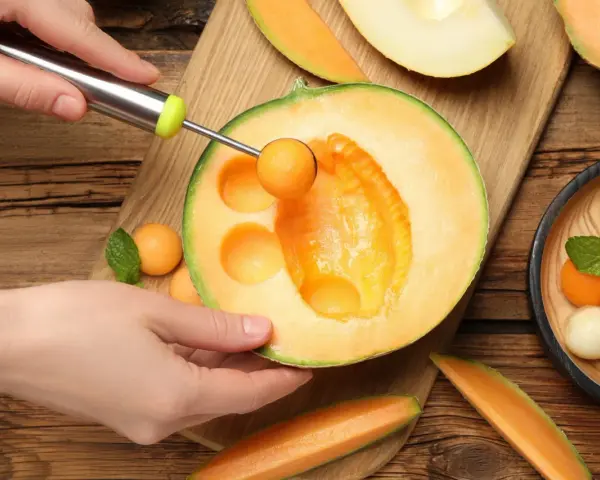 Ręka z gałkownicą wydobywa kulki z melona, ukazując jego soczyste wnętrze. Melon właściwości odżywcze czynią go idealnym na letnie orzeźwienie.