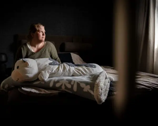 En kvinna sitter i sängen med en stor kramdjursko. Hon ser ut att fundera, kanske över sina två personligheter.