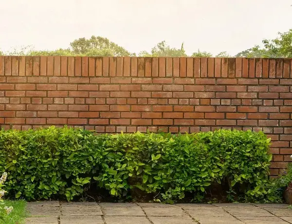 Eine Ziegelmauer im Garten, umgeben von üppigem Grün und blühenden Pflanzen. Tolle Ideen für Gartenmauern, die Privatsphäre und Schönheit vereinen.