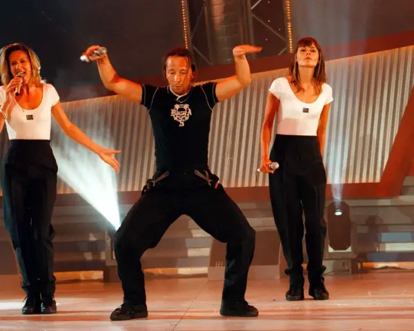 Drei Künstler in Schwarz-Weiß-Outfits performen auf einer Bühne. Die Frau links singt, der Mann in der Mitte tanzt, die Frau rechts hält ein Mikrofon. Ein energiegeladener Moment für **dance & electronic** Musik.