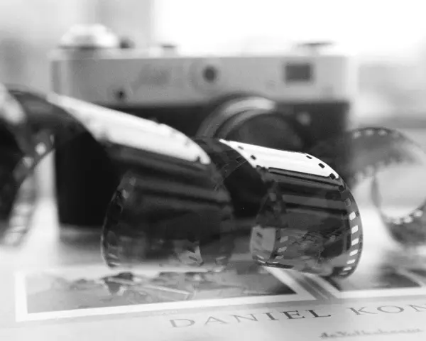 Analogowa fotografia: zwoje kliszy filmowej przed aparatem, na tle książki z napisem "DANIEL KONI".