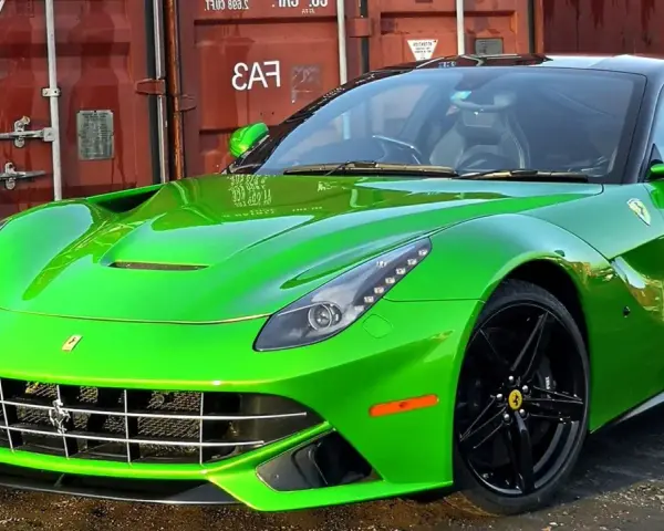 Jaskrawozielone Ferrari F12 Berlinetta z czarnymi felgami, zaparkowane przed czerwonym kontenerem.