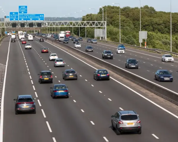 Autostrada z ruchem lewostronnym, pełna samochodów i ciężarówek. Znaki drogowe wskazują M1, A405 i M25.