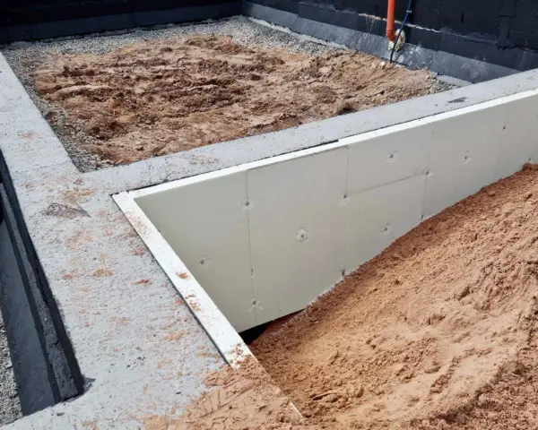 Fundament pod altanę w budowie: betonowe ławy, izolacja ze styropianu i nasypy ziemi. Słupki fundamentowe pod altanę czekają na montaż.