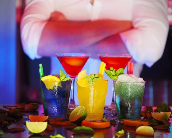 Kolorowe drinki z owocami i miętą na barze, w tle barman.