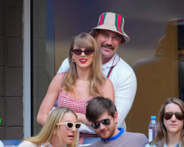 Travis Kelce e Taylor Swift sorridono, lei con un vestito a quadri rossi, lui con un cappello Gucci.