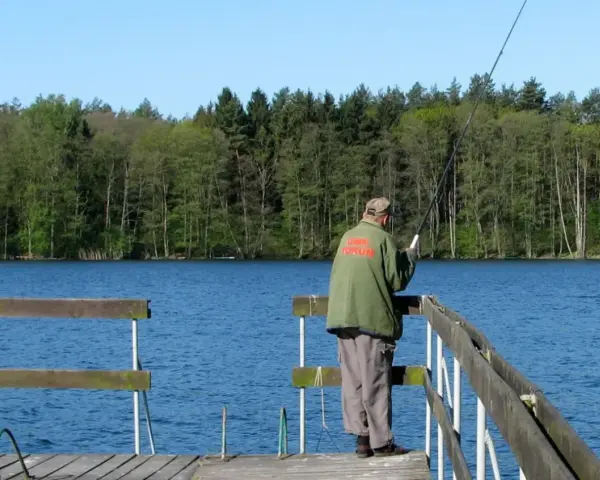Wędkarz na pomoście nad spokojnym zalewem Koronowskim, w tle las.