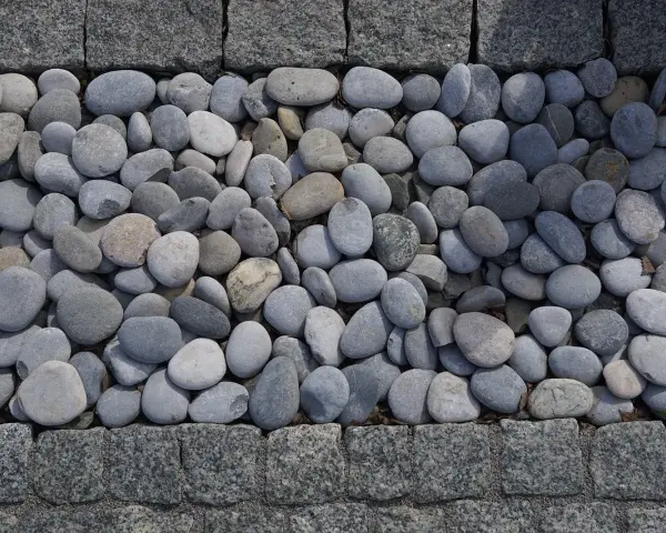 Gładkie, szare kamienie tworzą naturalną dekorację w ogrodzie, otoczone granitową kostką.