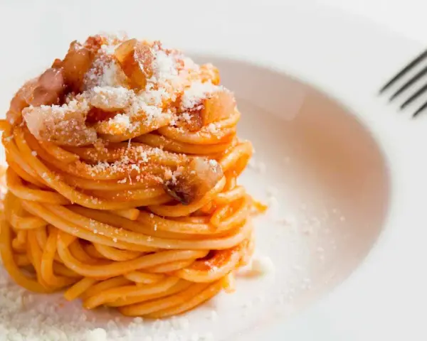 Un piatto di spaghetti alla amatriciana ricetta, conditi con guanciale croccante e pecorino grattugiato, pronti per essere gustati.