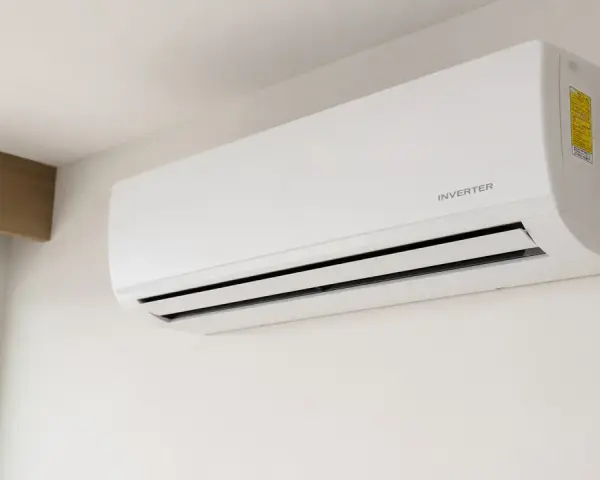 Unidad de aire acondicionado blanca con tecnología inverter, montada en pared blanca, cerca de una ventana.