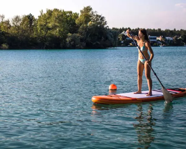 Frau genießt das sub fahren auf einem ruhigen See, umgeben von grünen Bäumen und Häusern.