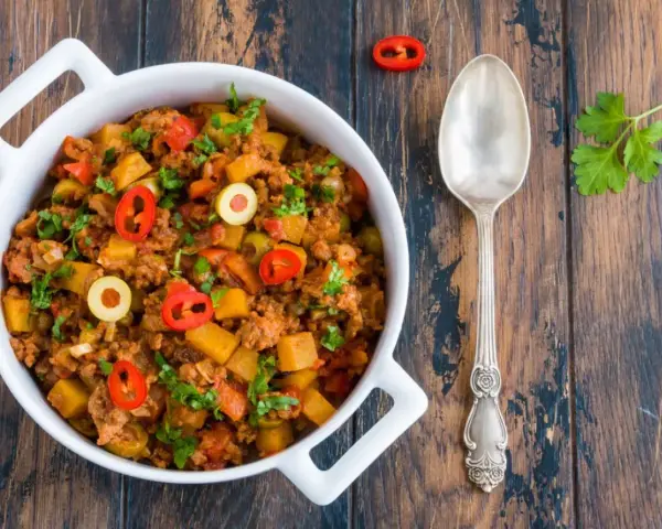 Pyszne danie z mielonego mięsa wołowego z ziemniakami, oliwkami i papryczką chili, posypane natką pietruszki.