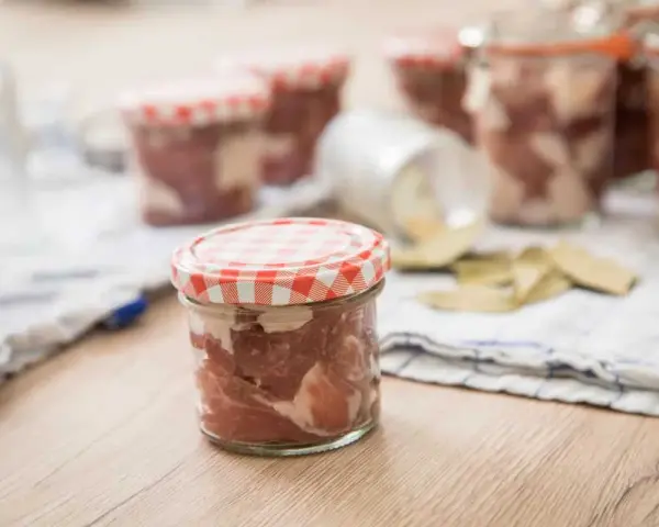 Słoiki z mięsem, przygotowane do tyndalizacji. Na stole leżą też liście laurowe.