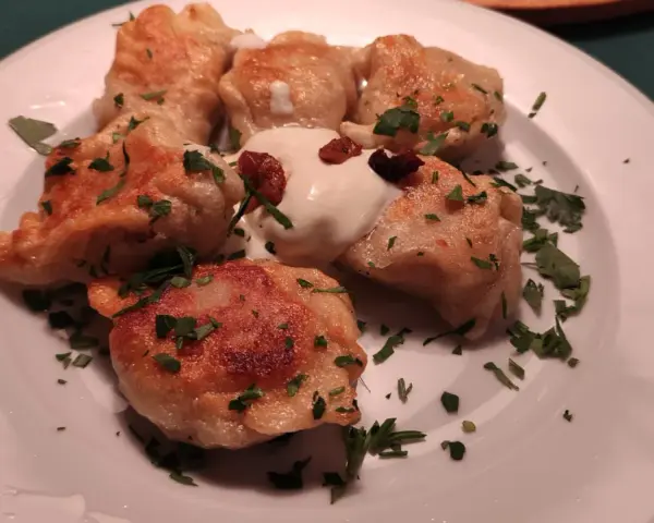 Pierogi, un piatto tipico polacco, serviti su un piatto bianco con panna acida e prezzemolo tritato.