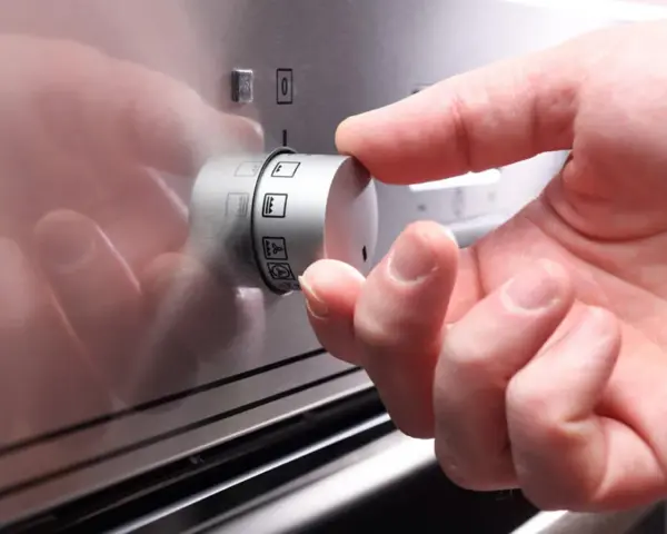 Ein Finger dreht am Drehregler, um die Heizart für den Backofen einzustellen. So funktioniert ein Backofen: Wahl der richtigen Funktion.