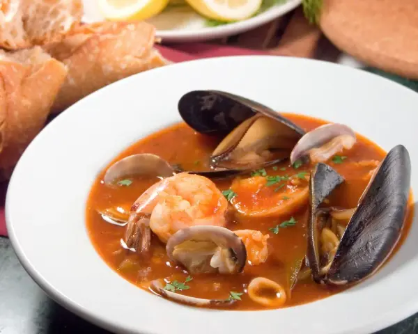 Sopa de mariscos en plato blanco con mejillones, camarones, almejas y pan.