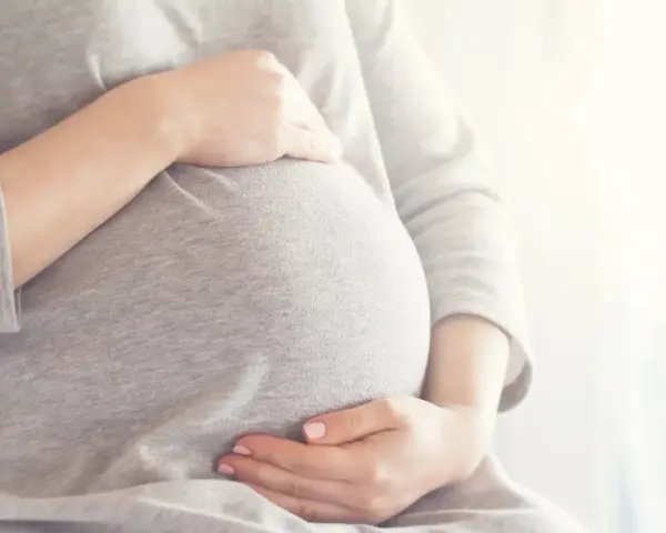 Brzuszek w 6 miesiącu ciąży, delikatnie otulony dłońmi.