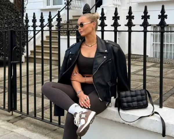 Kobieta w skórzanej kurtce i legginsach, uosobienie stylu athleisure, siedzi na murku przed kamienicą.