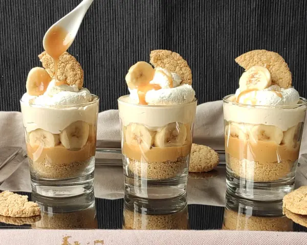 Pyszny deser bananowy przepis w szklaneczkach: warstwy ciastek, karmelu, bananów i bitej śmietany. Idealny na deser!