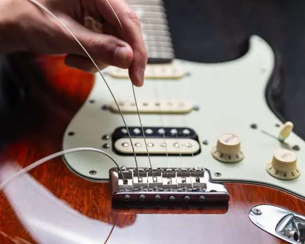 Dłoń naciąga nowe struny w gitarze elektrycznej, przygotowując ją do gry.