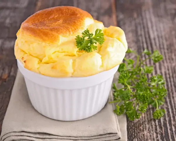 Un soufflé au fromage doré et gonflé, garni de persil frais, dans un ramequin blanc sur une serviette grise.