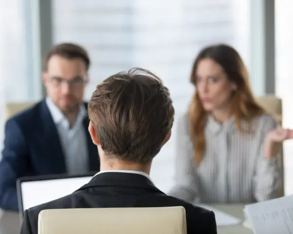 Besprechung mit einem Anwalt über Versicherungsansprüche. Eine Frau gestikuliert, während ein Mann mit Brille und ein Mann im Vordergrund zuhören.